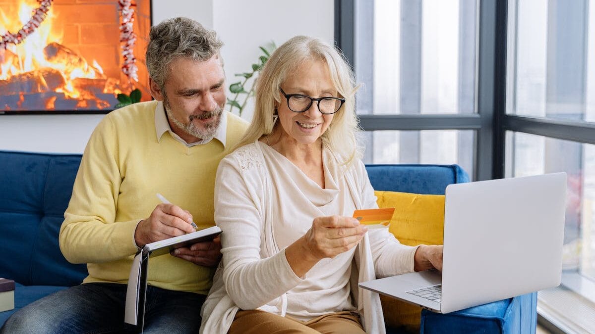 A couple sitting on a couch with a laptop and a credit card.