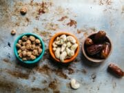 Three bowls of nuts and dates on a metal surface.