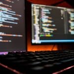 A computer with two monitors and a keyboard showing some programming codes.