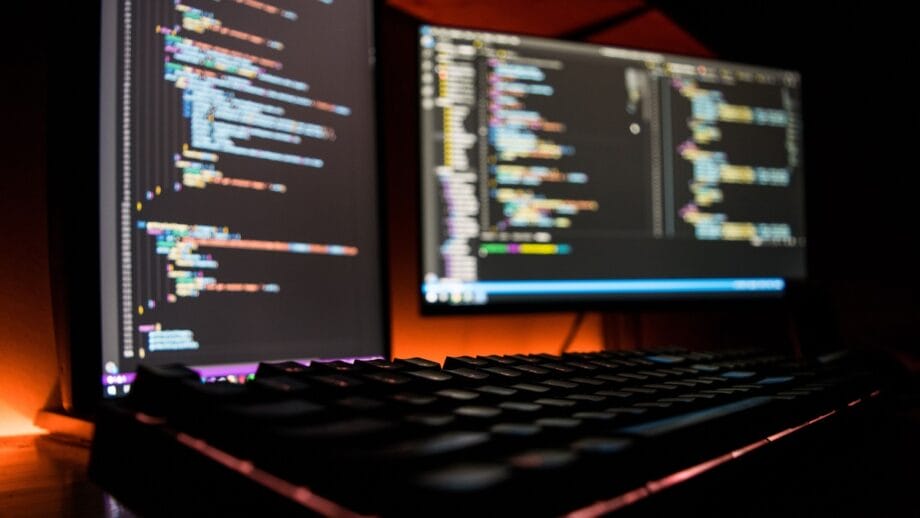 A computer with two monitors and a keyboard showing some programming codes.