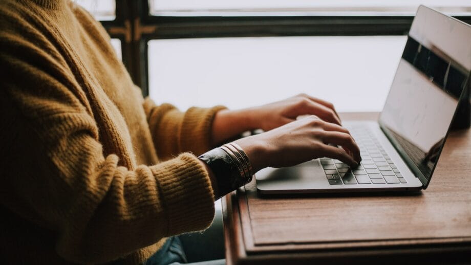 A woman typing on a laptop in front of a window.