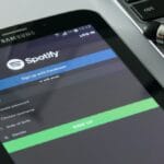 A Samsung tablet displays the Spotify sign-up page next to a laptop and a pair of black earphones.