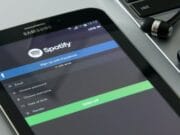 A Samsung tablet displays the Spotify sign-up page next to a laptop and a pair of black earphones.