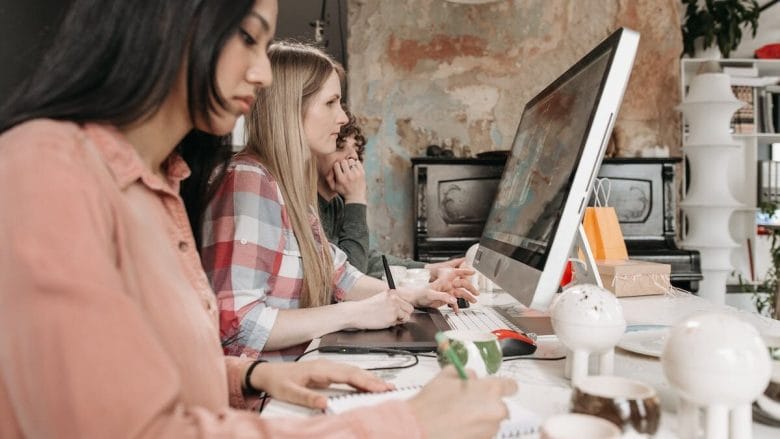 Three people working on a computer in an office.