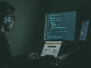 A man sitting in front of a computer screen in the dark.