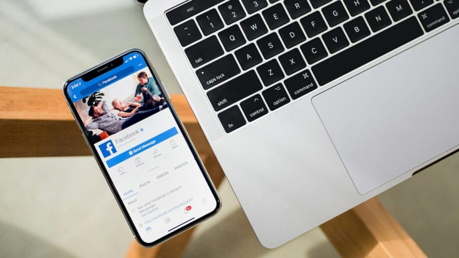 A laptop and a smartphone placed on a wooden table showing Facebook app.