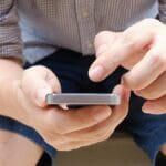 A person seated on a wooden bench is using a smartphone with both hands.