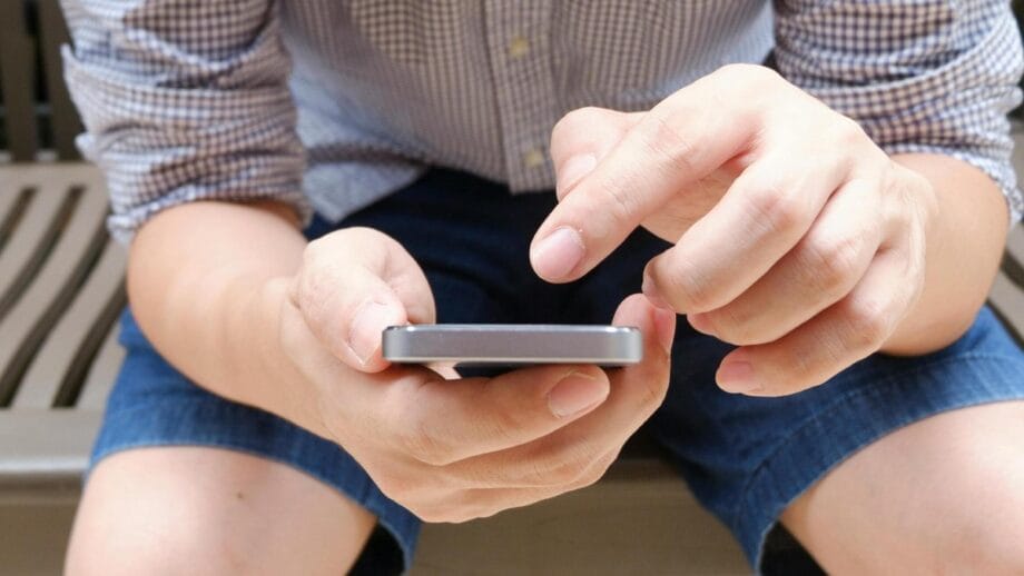 A person seated on a wooden bench is using a smartphone with both hands.