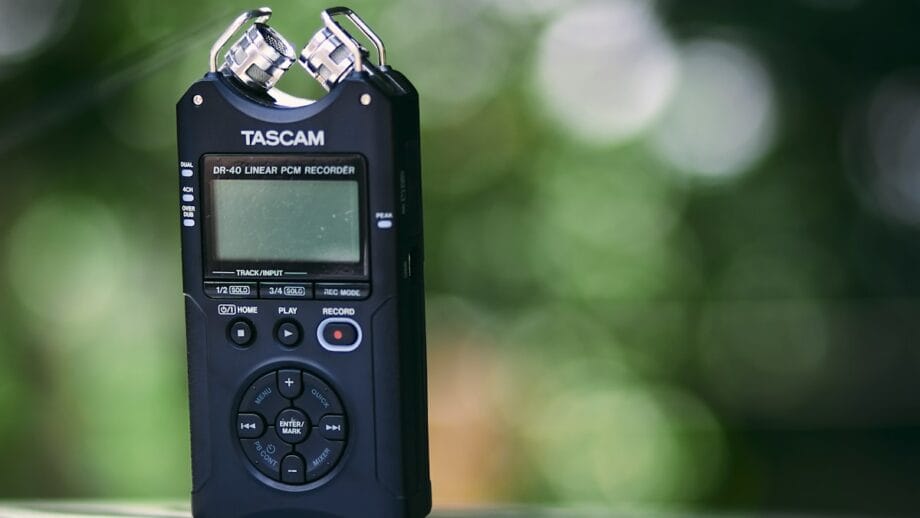 A tascam dr-40 linear pcm recorder standing on a reflective surface with a blurred green background.