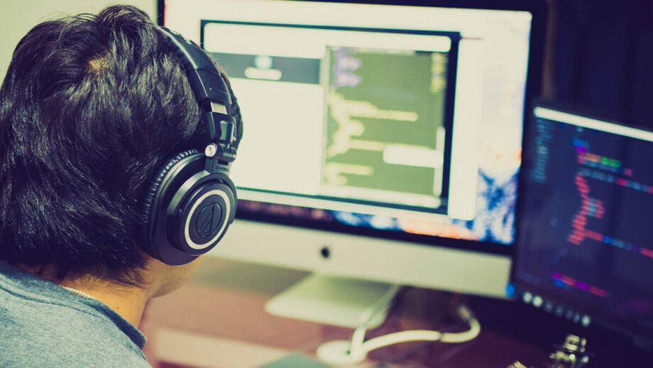 A person with headphones is working on a computer with multiple screens displaying code.