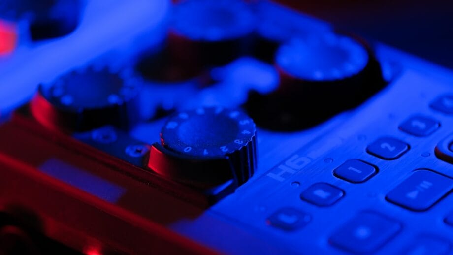 Close-up of a digital audio recorder's control surface illuminated by blue light, highlighting its buttons and dials.