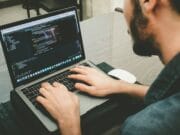 Man working on a laptop with code on the screen.