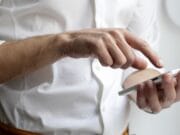 A person in a white shirt is using a smartphone with one hand, interacting with the screen via touch.