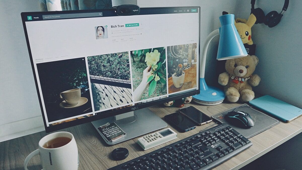 A well-organized desk with a computer displaying a social media profile, surrounded by various office items including a cup of coffee, headphones, a notepad, a smartphone, a calculator, and some decorative objects.