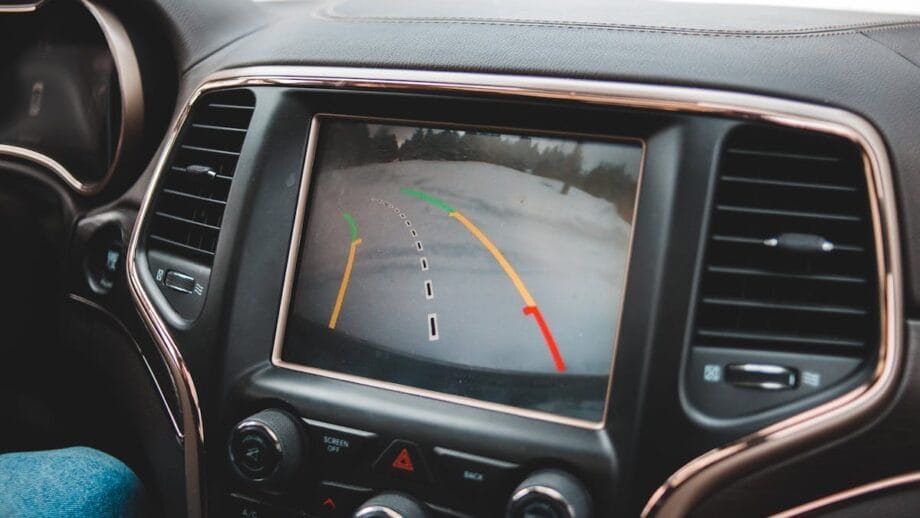 Car's dashboard view showing a rear-view camera display with dynamic parking lines indicating a snowy road behind the vehicle.