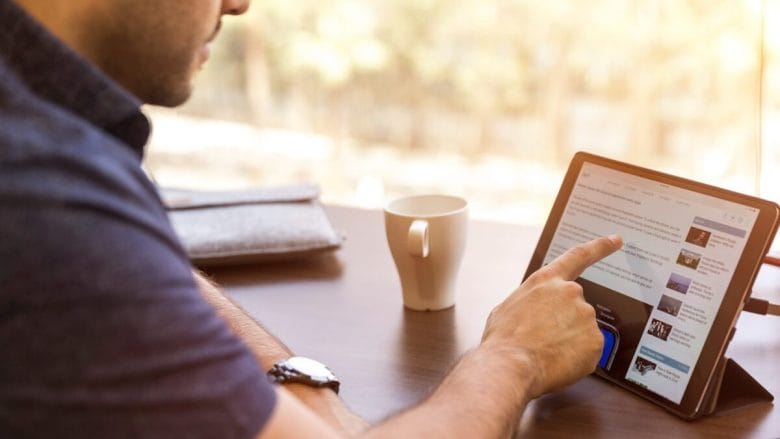 A person sitting at a table interacts with a digital tablet, while a coffee cup rests nearby.