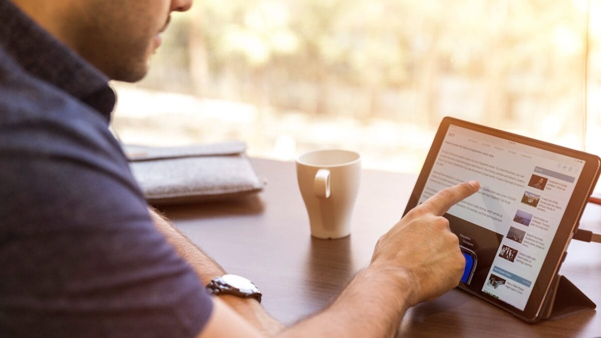 A person sitting at a table interacts with a digital tablet, while a coffee cup rests nearby.