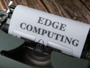 An old-fashioned typewriter with a sheet of paper that reads "edge computing" in bold, uppercase letters, set against a rustic wooden background.