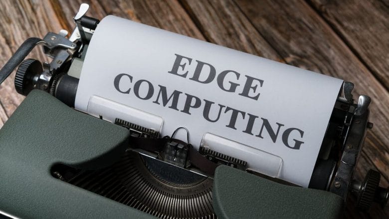 An old-fashioned typewriter with a sheet of paper that reads "edge computing" in bold, uppercase letters, set against a rustic wooden background.