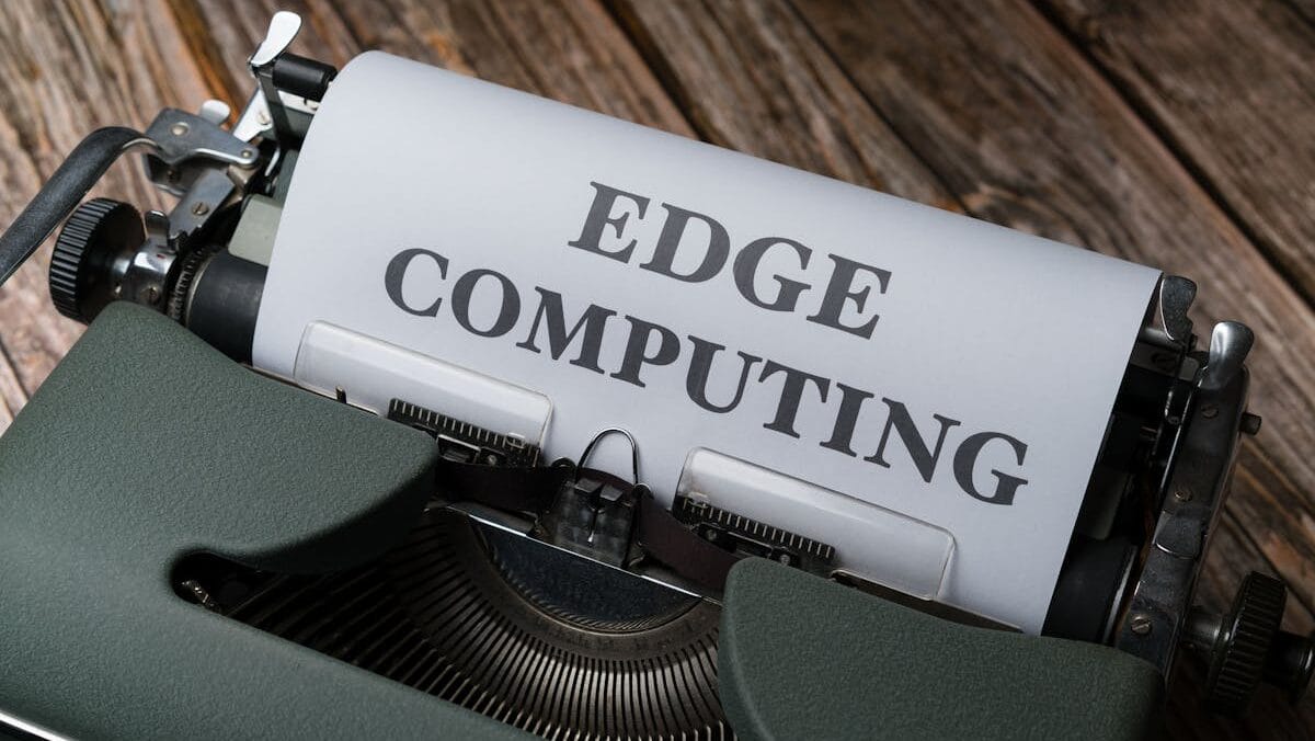 An old-fashioned typewriter with a sheet of paper that reads "edge computing" in bold, uppercase letters, set against a rustic wooden background.