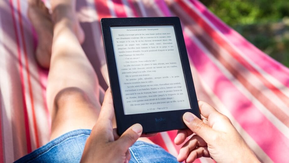 A person reclining on a hammock is reading an e-book on a tablet.