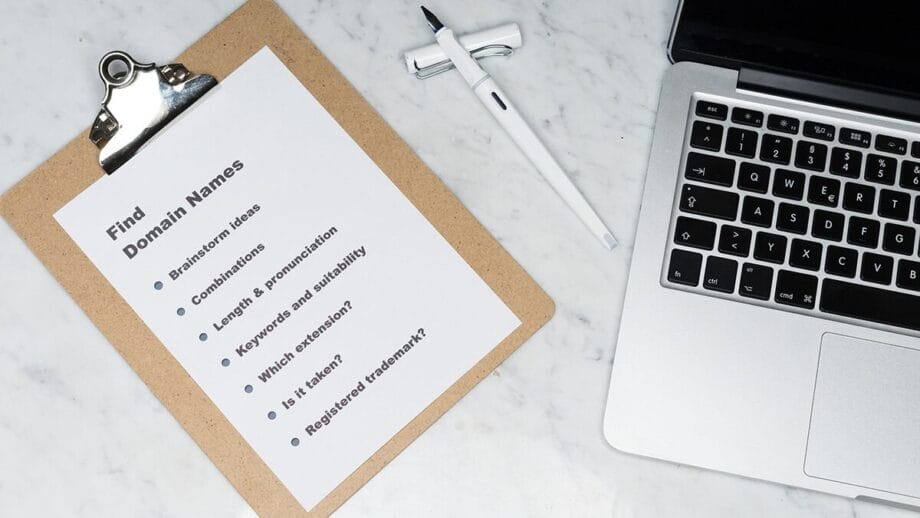 A clipboard with a list titled "Find Domain Names" beside a pen and a laptop on a white surface.