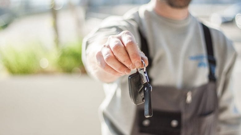 A man in a gray uniform holds out a set of car keys, focusing the camera on the keys with a softly blurred background.