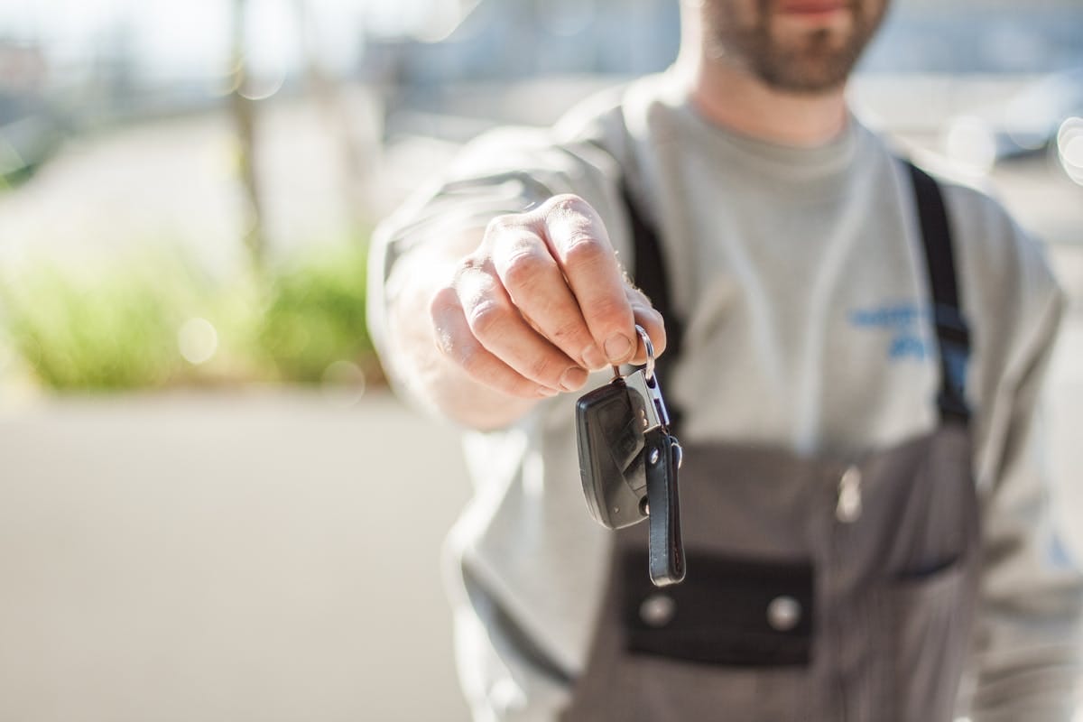 A man in a gray uniform holds out a set of car keys, focusing the camera on the keys with a softly blurred background.