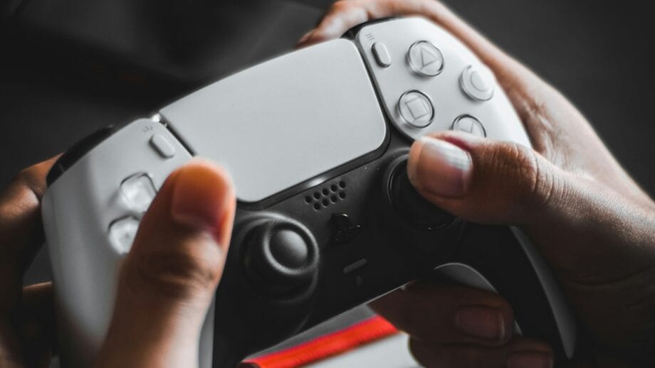Close-up of hands holding a white PlayStation controller with a blurred background.