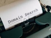 A green typewriter with a sheet of paper displaying the words "Domain Search.
