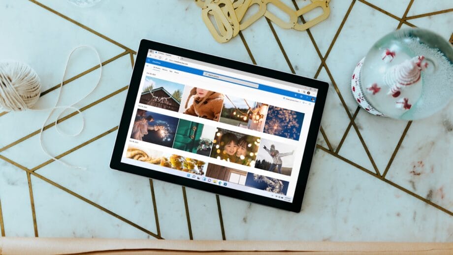 A tablet displaying a photo gallery is placed on a geometric pattern table next to a snow globe, beige yarn, a water bottle, and some gold keychains.