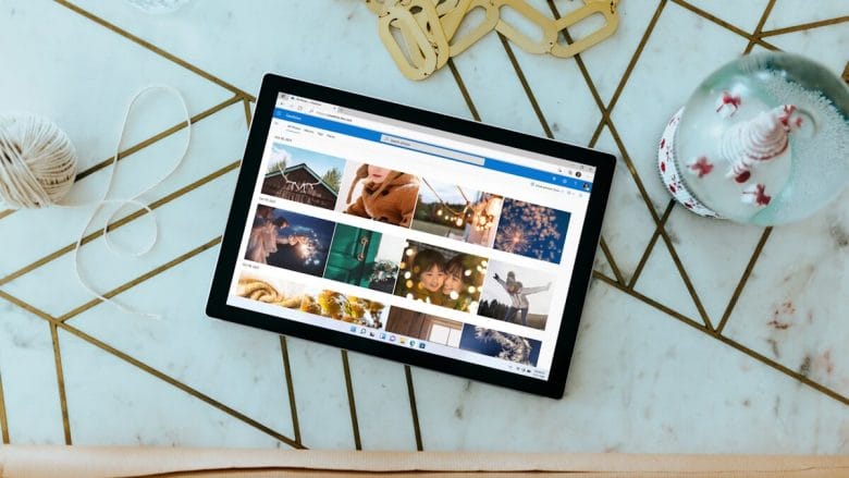 A tablet displaying a photo gallery is placed on a geometric pattern table next to a snow globe, beige yarn, a water bottle, and some gold keychains.