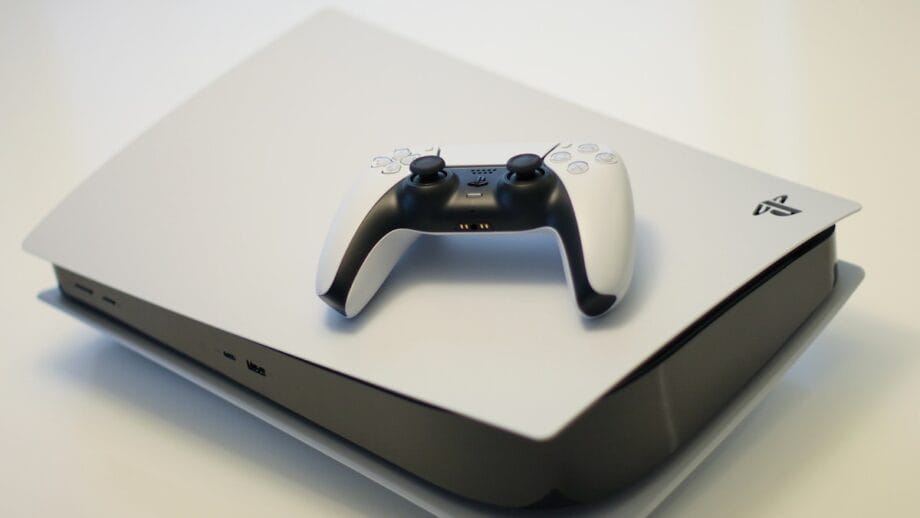A PlayStation 5 console with a DualSense controller placed on top. The console is white with black accents.