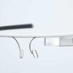 A close-up view of a pair of smart glasses with a lightweight, minimalist design, featuring a small rectangular display on one side, nose pads, and a thin frame.