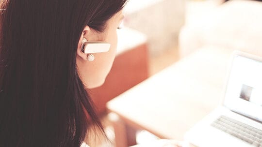 Person wearing a headset, looking at a laptop screen in a bright room.