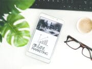 A tablet displaying "online marketing" lies on a white desk next to a plant, glasses, a coffee cup, and a black keyboard.