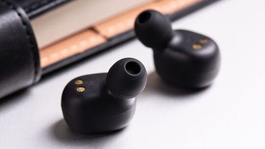 Two black wireless earbuds placed on a surface near a leather wallet or case.