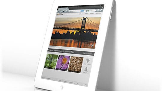 A white tablet with a website open, displaying a photo of a sunset behind a bridge, and thumbnails of flowers, tree bark, and a heart symbol below.