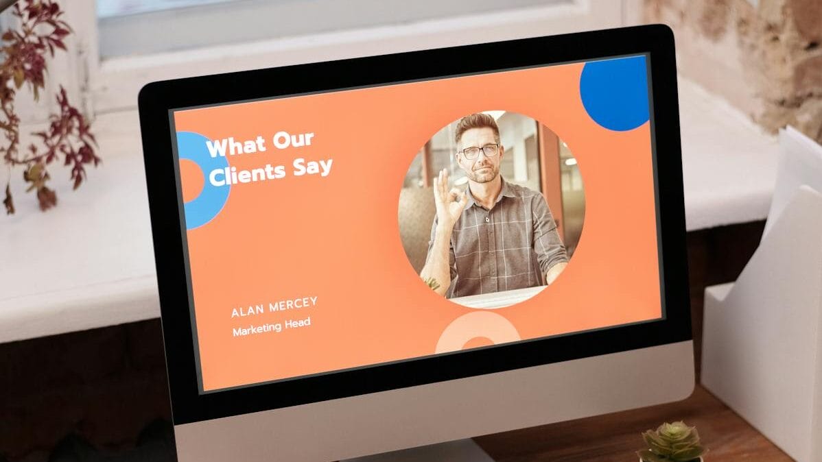 Computer monitor displaying a slide titled "What Our Clients Say" with a portrait of a man identified as Alan Mercey, Marketing Head.