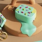 AirPods Pro case designed to look like a melting ice cream bar with colorful sprinkles and a keyring attachment, placed on a beige platform.