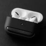 A pair of white wireless earbuds in a partially closed black charging case, resting on a plain dark surface.