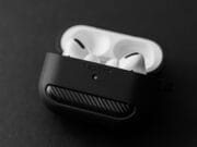 A pair of white wireless earbuds in a partially closed black charging case, resting on a plain dark surface.