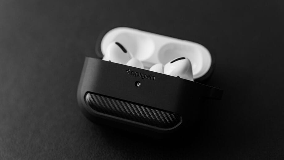 A pair of white wireless earbuds in a partially closed black charging case, resting on a plain dark surface.