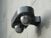 A black double dome security camera mounted on a gray concrete wall.