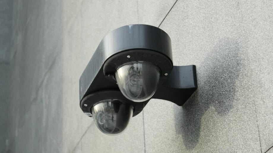 A black double dome security camera mounted on a gray concrete wall.