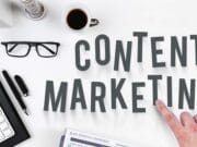 Desk with keyboard, glasses, coffee, and planner. Hand points at the words 'Content Marketing' in large letters.