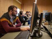 Several people are working at computers in an office setting, focusing on their screens and wearing headsets.