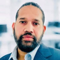 Raj Joseph, the author of this article, with a beard and mustache wearing a blue suit and white shirt, standing in an office environment.