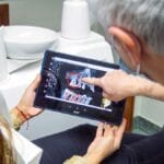 Dentist showing a patient dental X-rays on a tablet, pointing at specific areas.