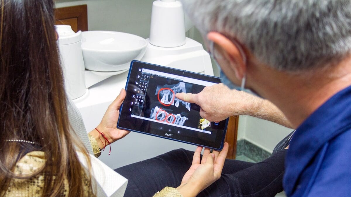 Dentist showing a patient dental X-rays on a tablet, pointing at specific areas.